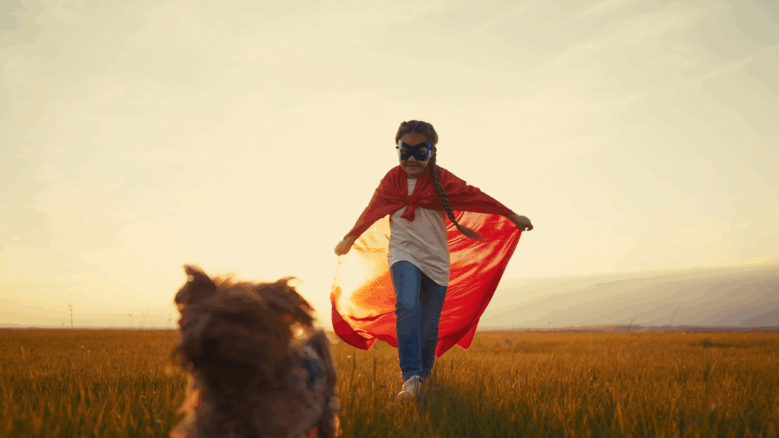 Child dressed as superhero chasing her pet dog through a field